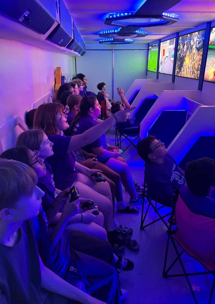 Teens pointing and reacting inside blue-lit gaming trailer
